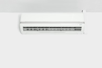 Photo of Modern air conditioner on white wall indoors. Space for text