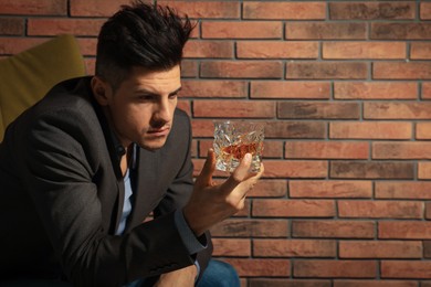 Addicted man with glass of alcoholic drink near red brick wall
