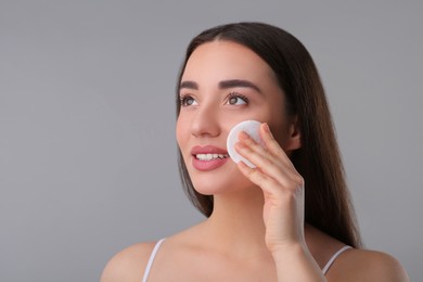 Photo of Beautiful woman removing makeup with cotton pad on gray background, space for text