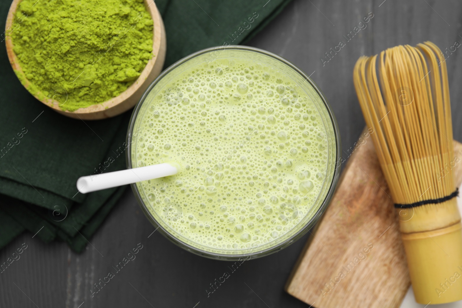 Photo of Glass of tasty matcha smoothie, powder and bamboo whisk on grey wooden table, flat lay