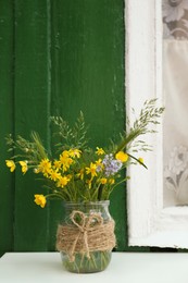 Bouquet of beautiful wildflowers in glass vase on table near window outdoors