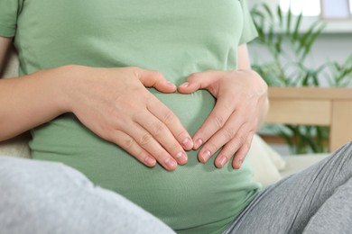 Pregnant woman making heart with her hands in room, closeup