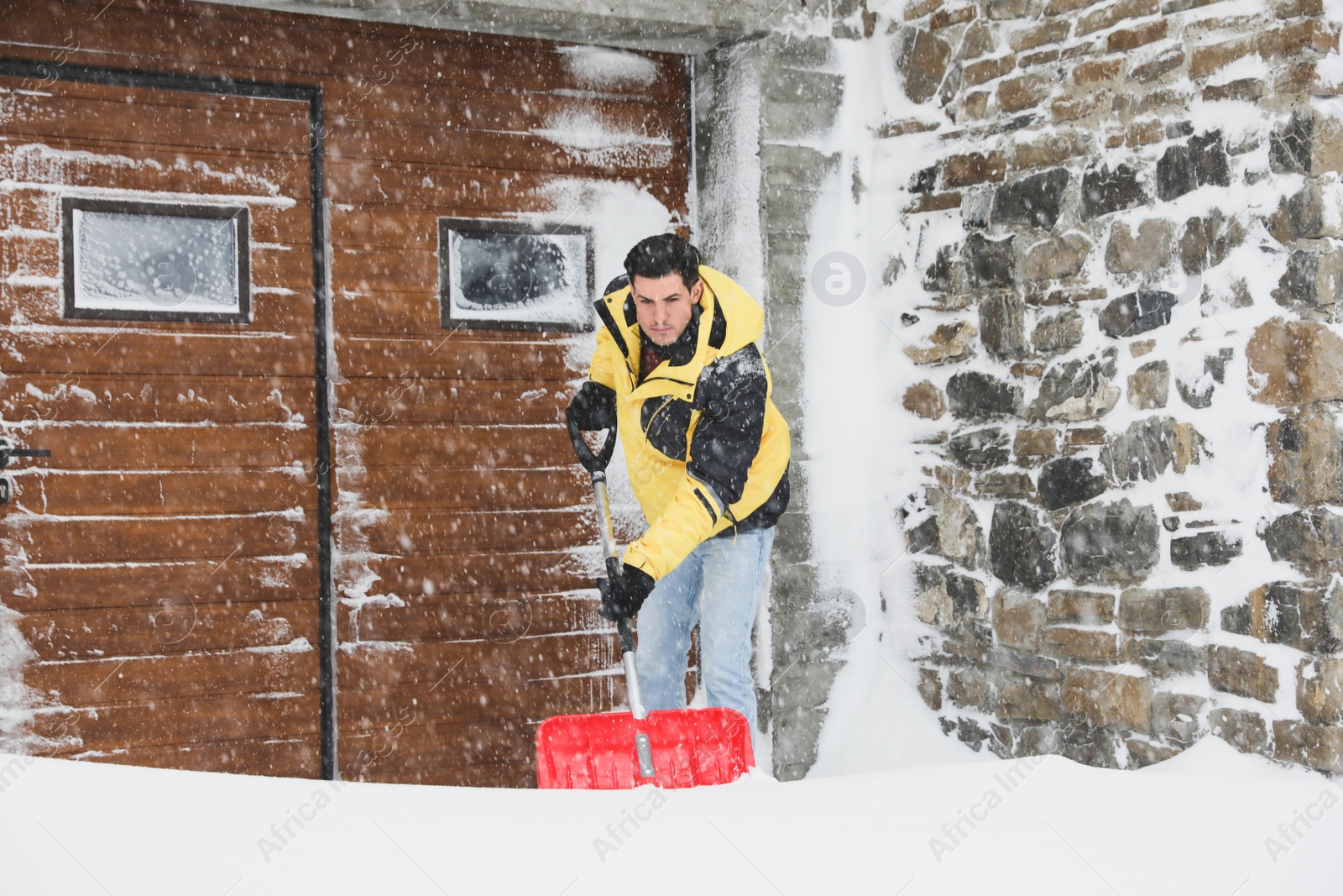 Photo of Man cleaning snow with shovel near his house