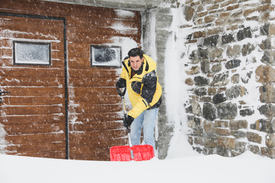 Photo of Man cleaning snow with shovel near his house