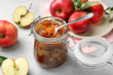 Photo of Tasty apple jam in glass jar and fresh fruits on light table