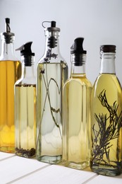 Photo of Bottles of different cooking oils on white wooden table against grey background