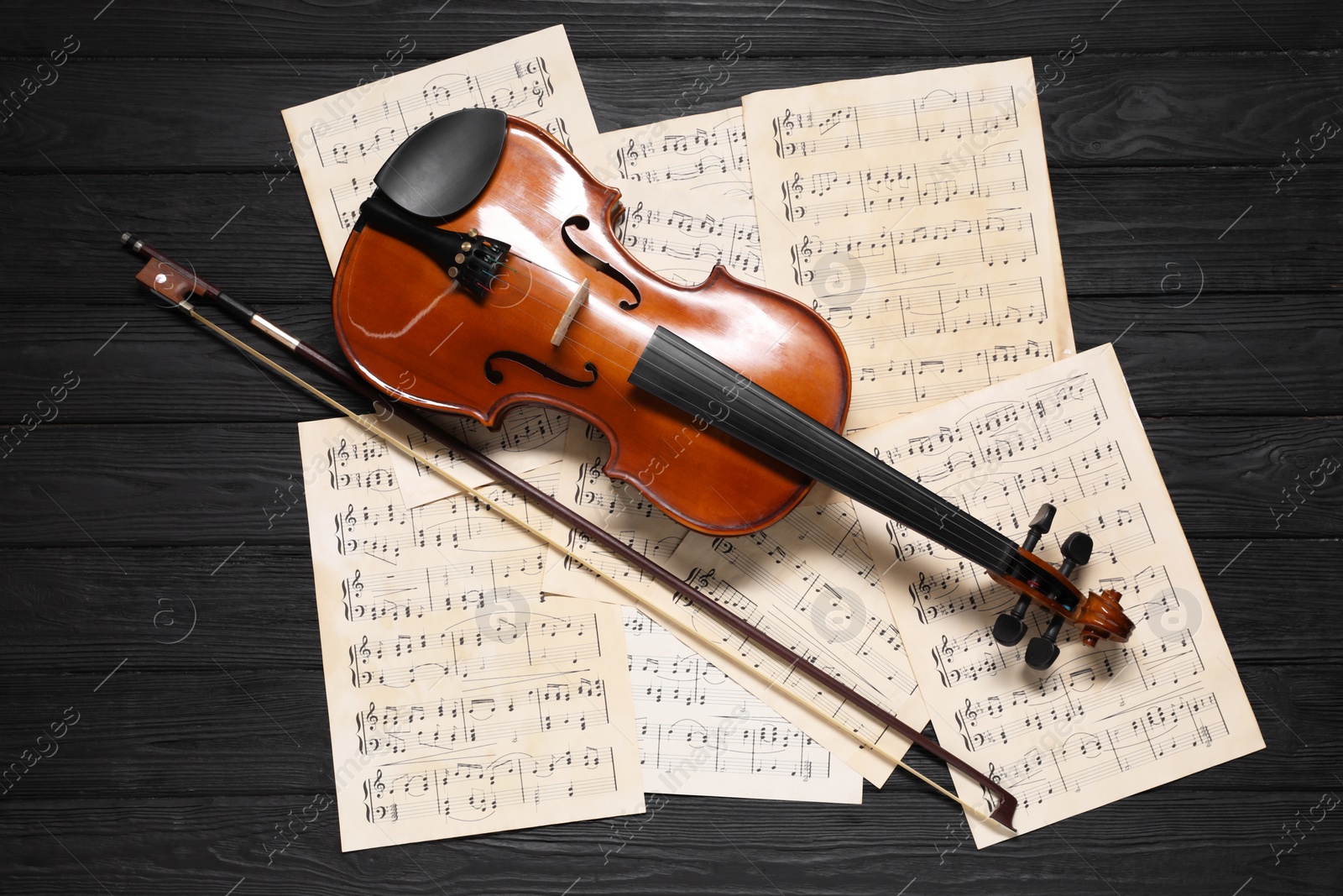 Photo of Violin, bow and music sheets on black wooden table, top view