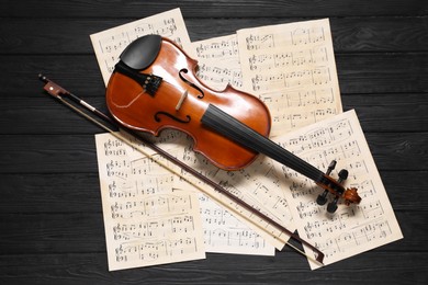 Violin, bow and music sheets on black wooden table, top view