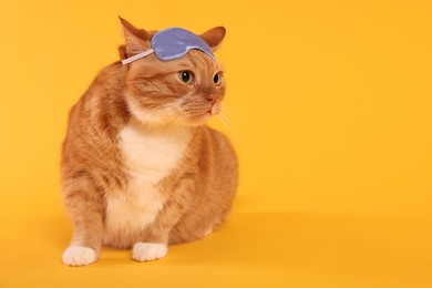 Cute ginger cat with sleep mask on orange background, space for text