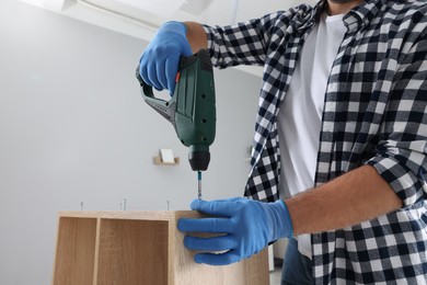 Photo of Man with electric screwdriver assembling furniture at home, closeup