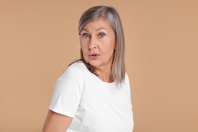 Portrait of surprised senior woman on beige background
