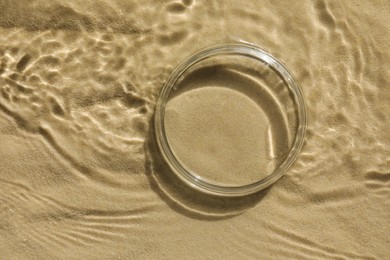 Photo of Stylish presentation for product. Glass podium in water on sand, top view