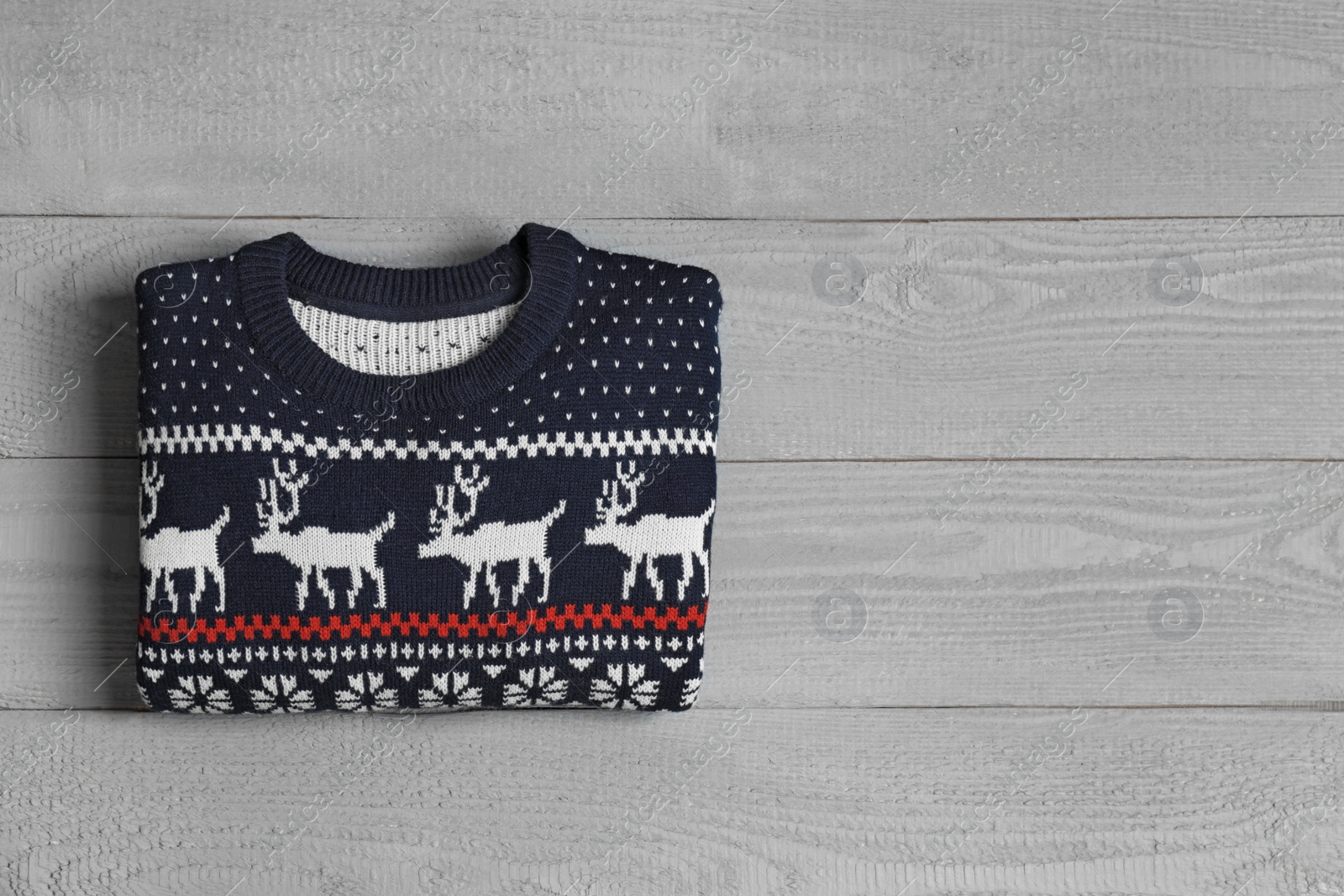 Photo of Warm folded Christmas sweater on grey wooden table, top view. Space for text