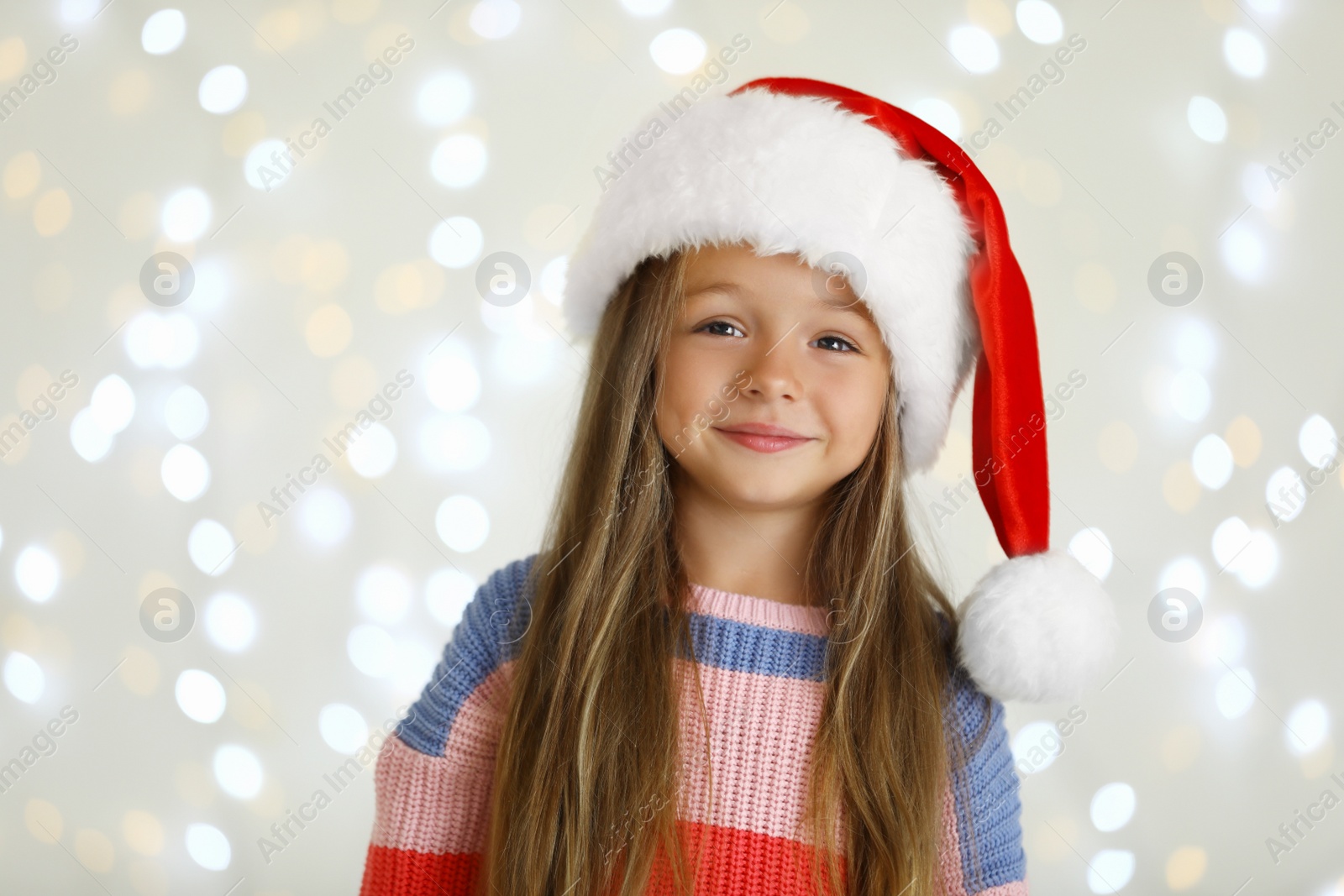 Photo of Happy little child in Santa hat against blurred festive lights. Christmas celebration