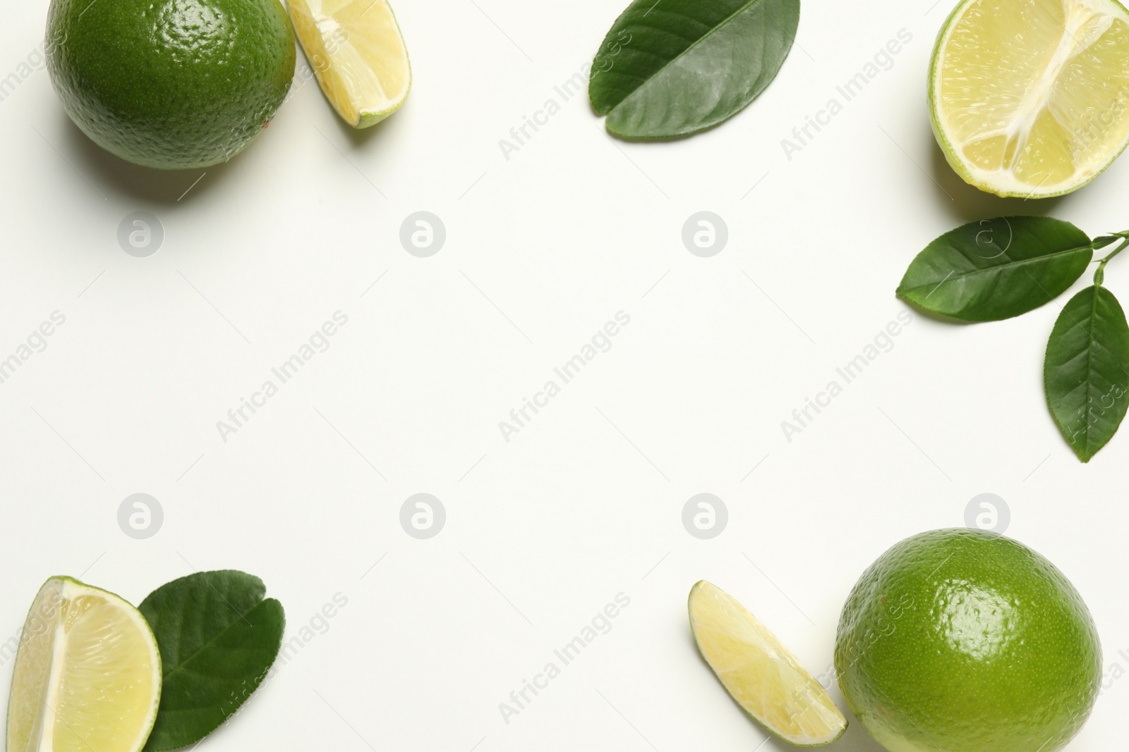 Photo of Whole and cut fresh ripe limes with green leaves on white background, flat lay