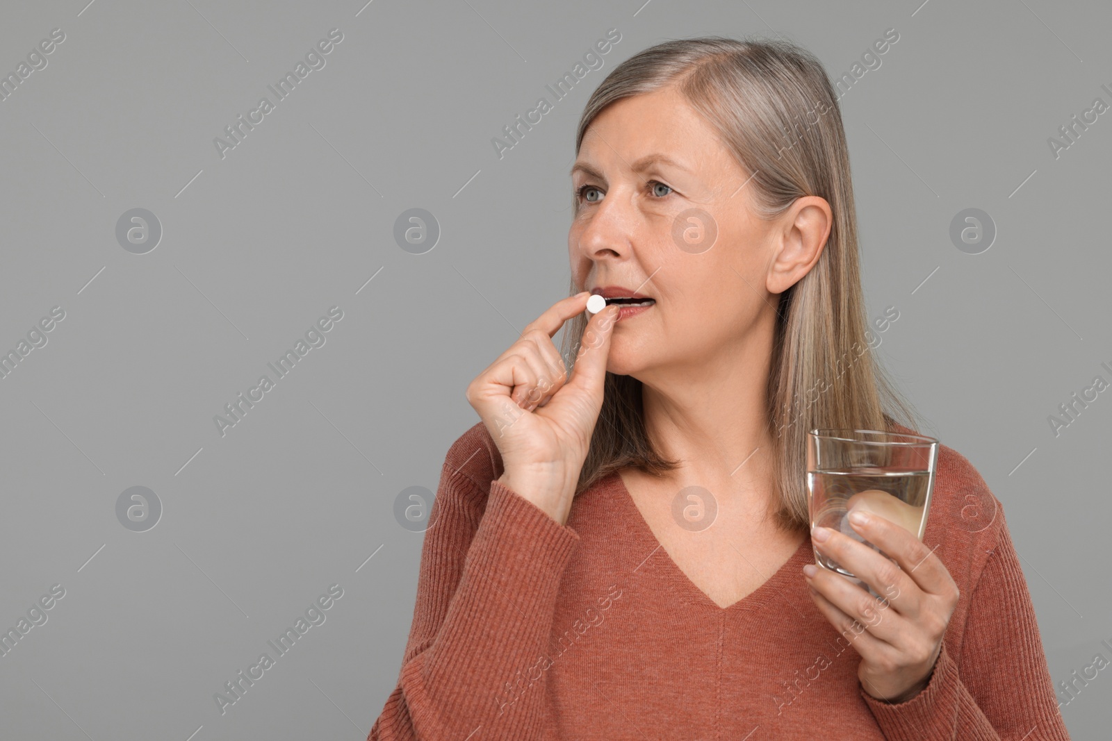 Photo of Senior woman with glass of water taking pill on grey background. Space for text