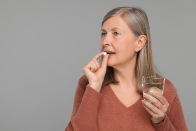 Senior woman with glass of water taking pill on grey background. Space for text