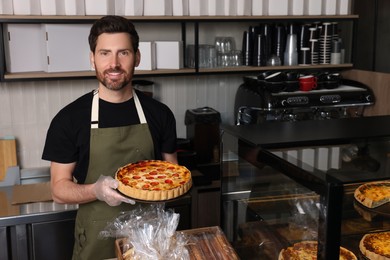 Photo of Seller with freshly baked quiche at cashier desk in bakery shop