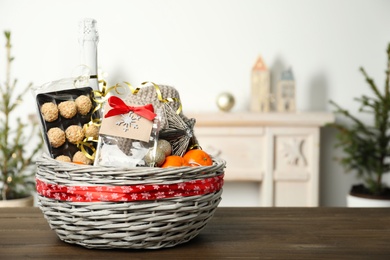 Photo of Wicker basket with Christmas gift set on wooden table. Space for text