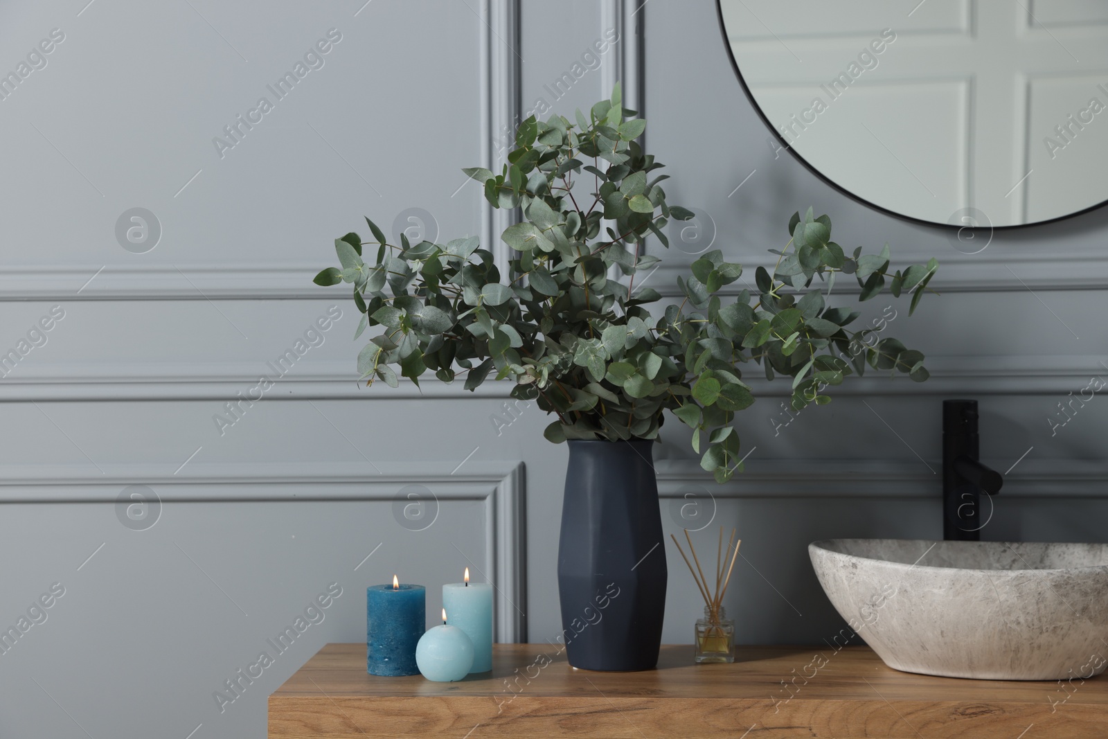 Photo of Burning candles, aroma sticks and eucalyptus branches near vessel sink on bathroom vanity, space for text. Interior design