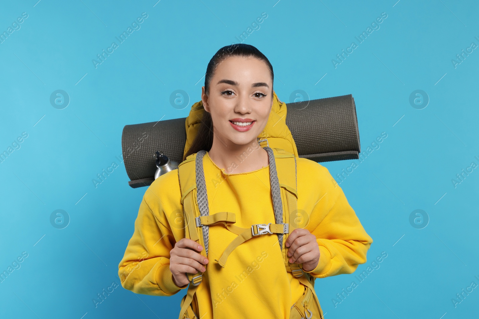 Photo of Smiling young woman with backpack on light blue background. Active tourism