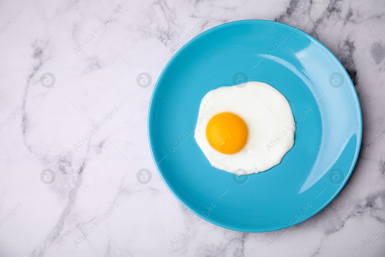 Photo of Tasty fried egg in plate on white marble table, top view. Space for text