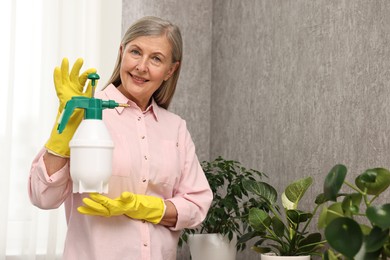 Photo of Happy housewife with plant mister near green houseplants at home