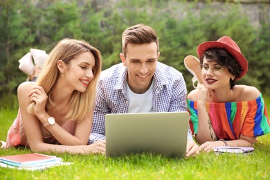 Group of friends in stylish clothes with laptop outdoors