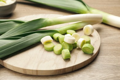 Photo of Whole and cut fresh leeks on wooden table, closeup