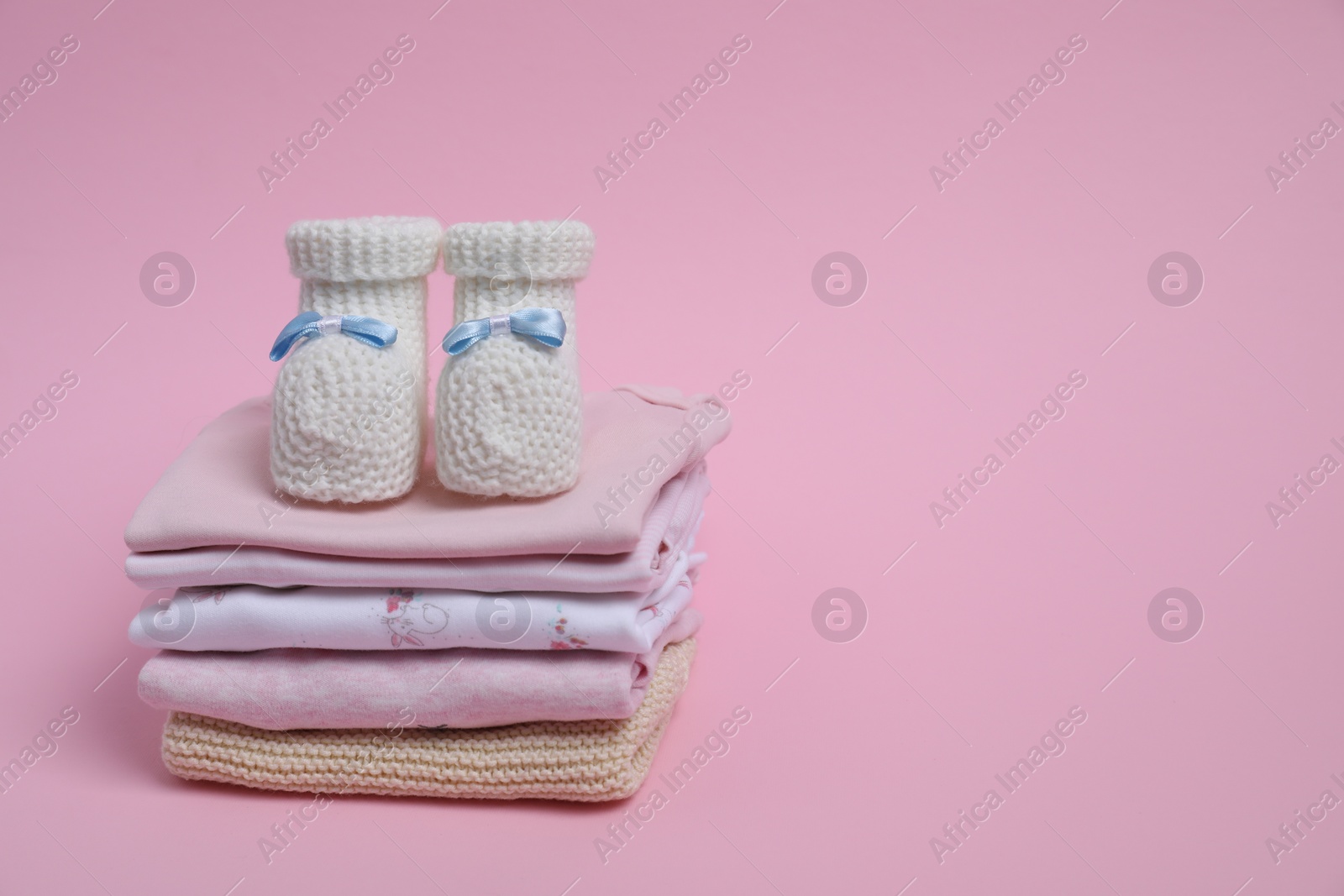 Photo of Stack of clean baby clothes and small booties on pink background. Space for text