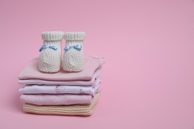 Photo of Stackclean baby clothes and small booties on pink background. Space for text