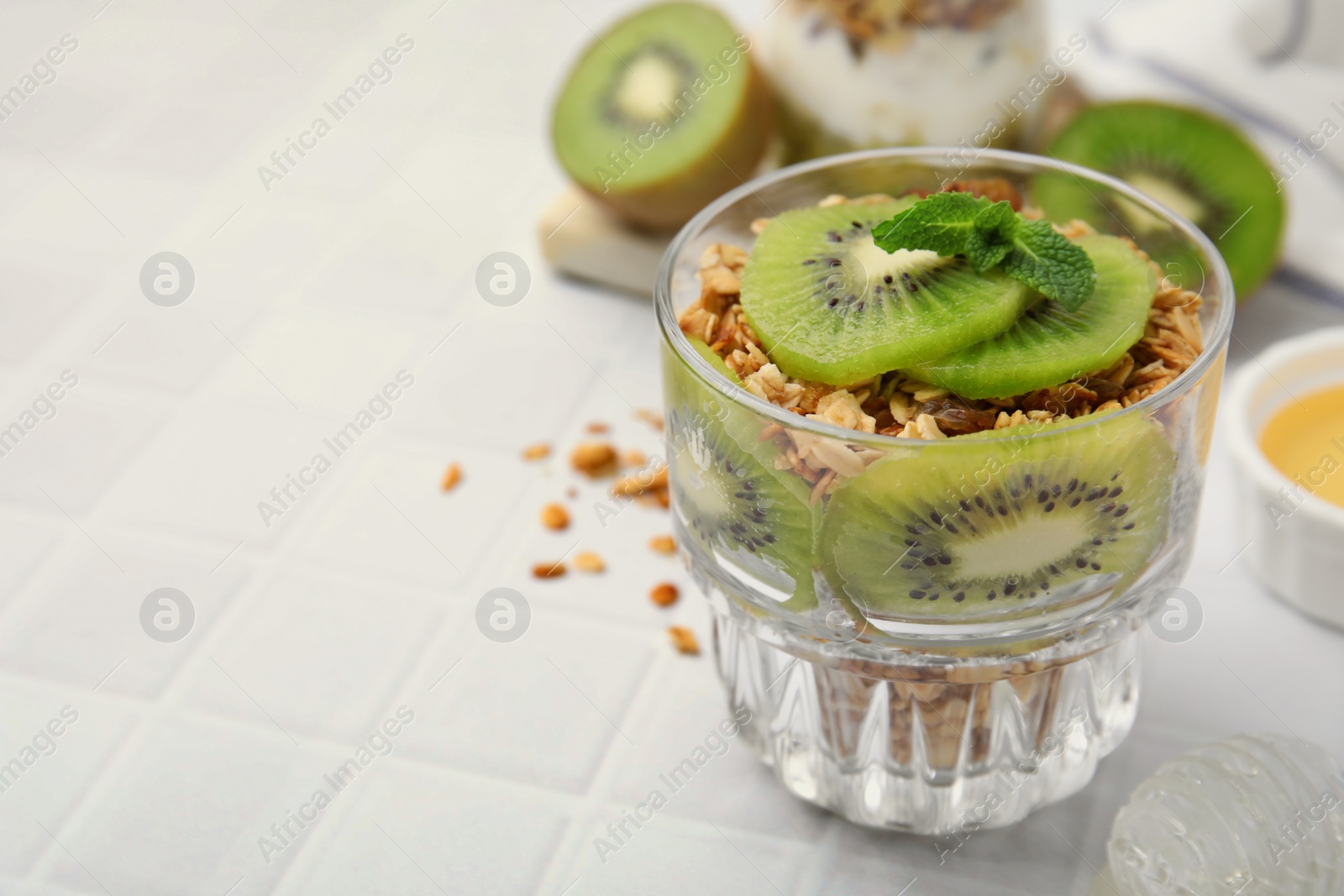 Photo of Delicious dessert with kiwi and muesli on white table, closeup. Space for text