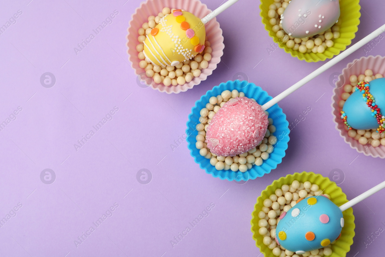 Photo of Egg shaped cake pops and space for text on violet background, flat lay. Easter celebration