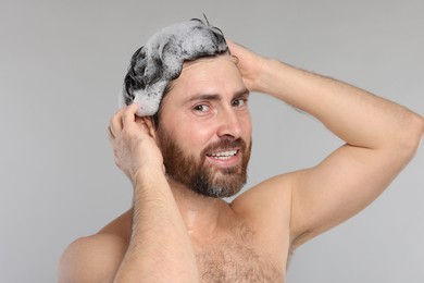 Happy man washing his hair with shampoo on grey background