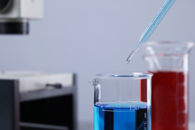 Photo of Dripping liquid from pipette into beaker in laboratory, closeup. Space for text