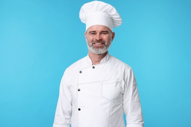 Photo of Happy chef in uniform on light blue background