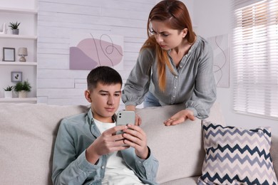 Photo of Mother scolding her son while he using smartphone at home. Teenager problems
