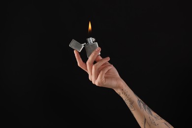 Photo of Woman holding lighter with burning flame on black background, closeup
