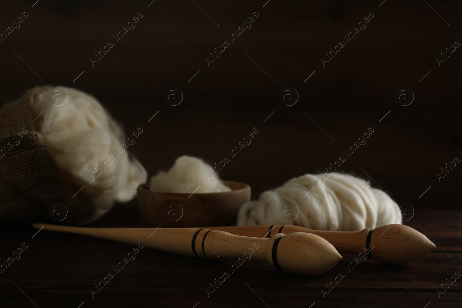 Photo of Soft white wool and spindles on wooden table, closeup