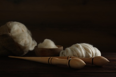 Photo of Soft white wool and spindles on wooden table, closeup