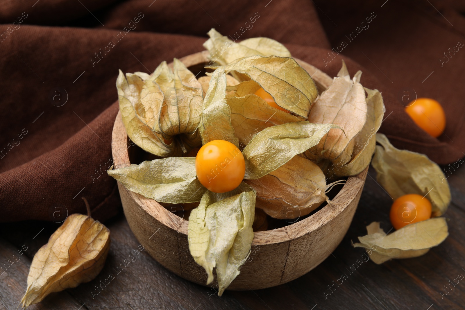 Photo of Ripe physalis fruits with calyxes in bowl on wooden table