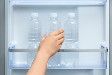 Photo of Woman taking bottle of water from refrigerator, closeup