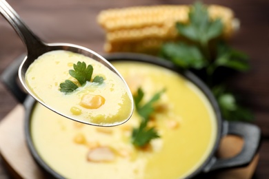 Spoon of delicious corn soup over full pot, closeup