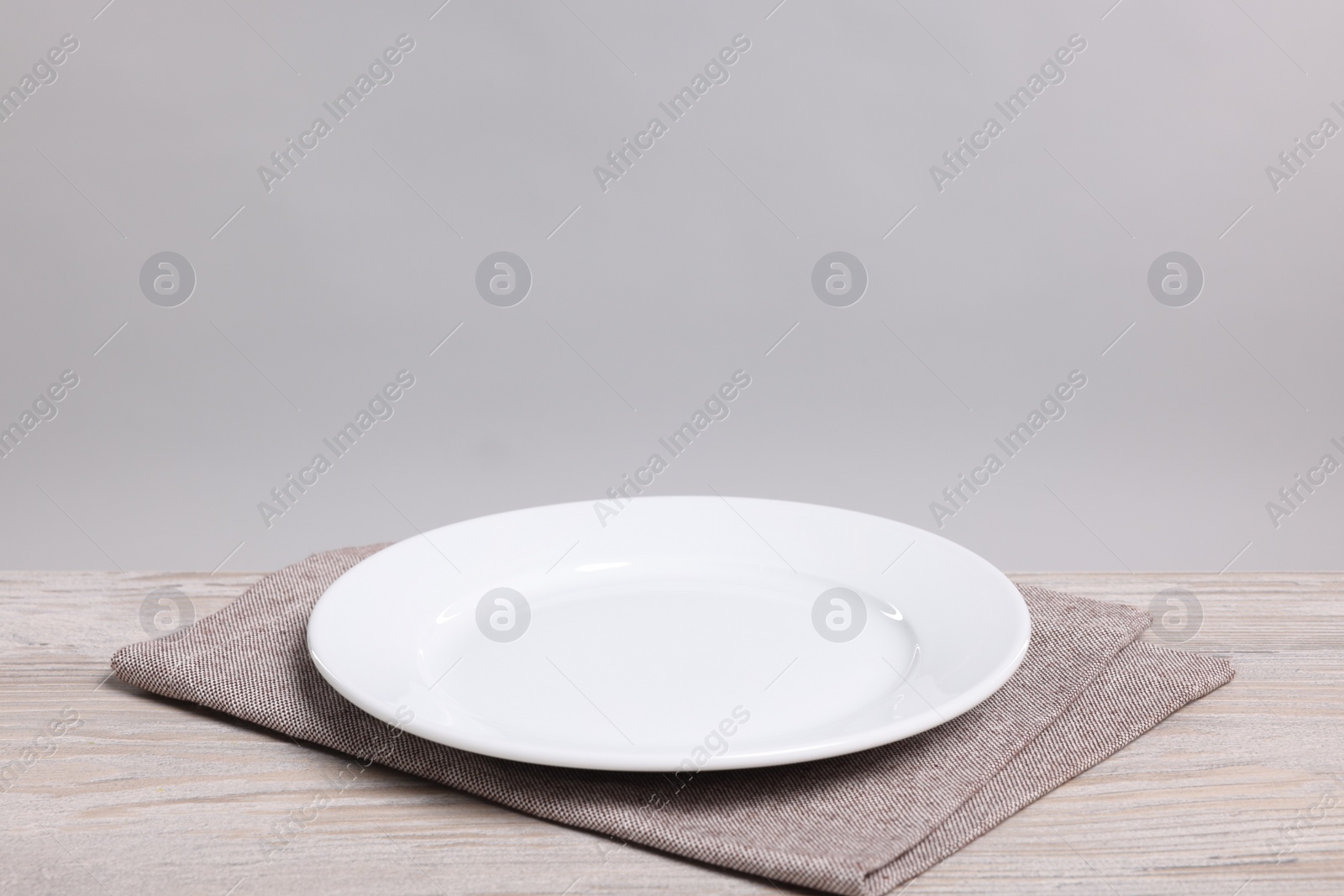 Photo of Empty ceramic plate on wooden table against light background, space for text