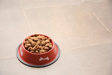 Dry dog food in feeding bowl on tiled floor. Space for text