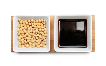 Wooden board with dishes of soy sauce and beans on white background, top view