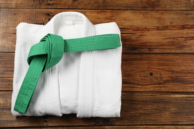 Photo of Green karate belt and white kimono on wooden background, top view. Space for text