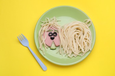 Photo of Creative serving for kids. Plate with cute dog made of tasty pasta, sausage and cucumber on yellow table, flat lay