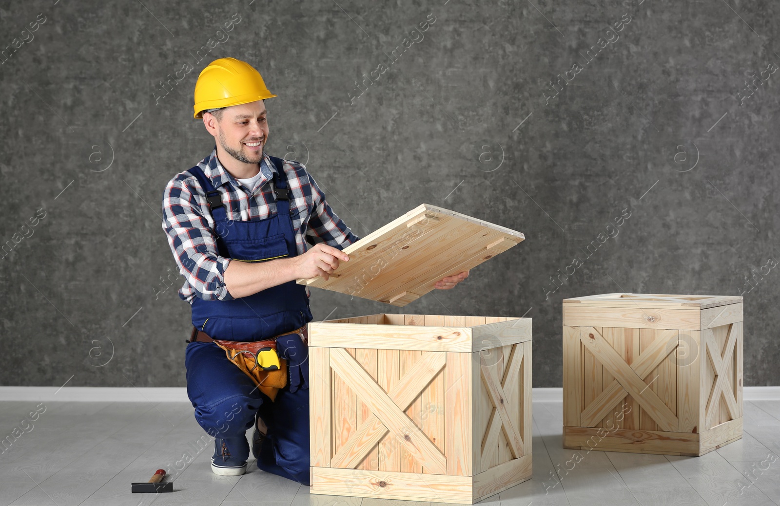Photo of Handsome man in hard hat working with wooden crate near color wall