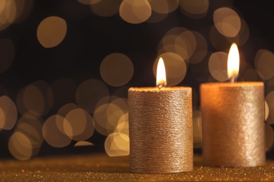 Photo of Burning gold candles on table against blurred lights. Space for text